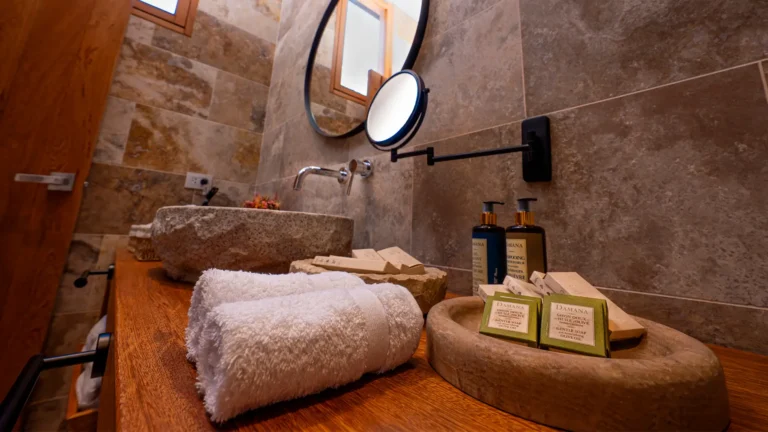 Tocador de madera fina con amenities de alta calidad, toallas blancas y un lavatorio artesanal de piedra en el baño del hotel boutique.