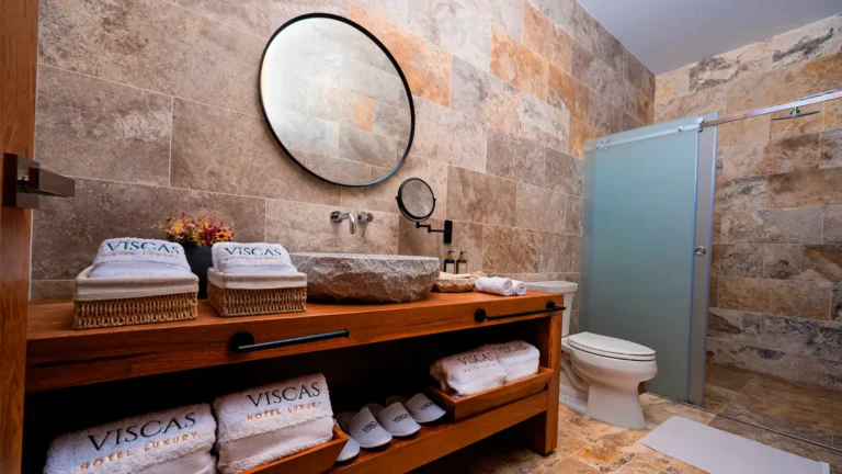 Baño de mármol de estilo rústico y elegante en una suite de Hotel Viscas, equipado con lavatorio de piedra, toallas premium y pantuflas de cortesía en Huaraz.